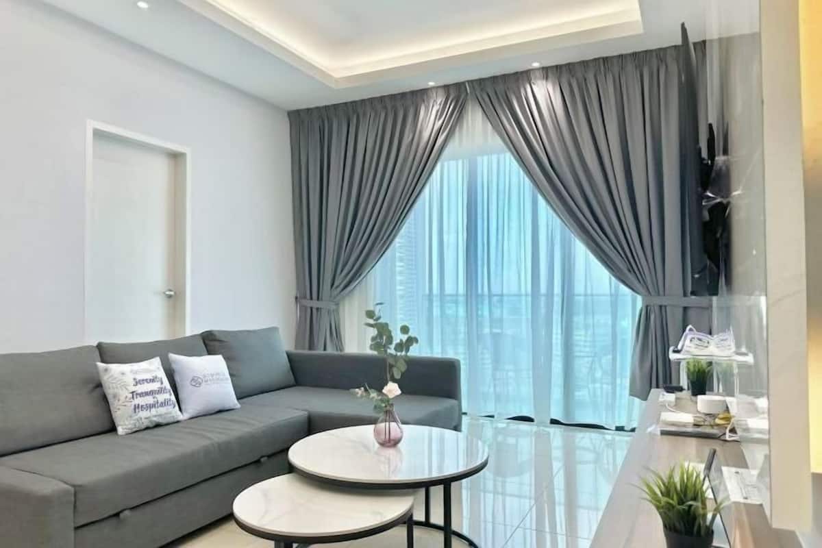 Ein modernes Wohnzimmer mit einem grauen Sofa, zwei runden Tischen, einer Blumenvase und einem großen Fenster mit grauen Vorhängen.