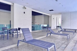 Un espace aménagé au bord de la piscine, avec des chaises longues et des tables, une paroi en verre et une vue sur la piscine.