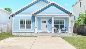 Une maison de plain-pied à l’extérieur bleu, avec un porche à l’avant doté de deux fauteuils en osier et un petit jardin.