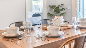 Une table à manger dressée avec de l’assiette, des bols et des couverts blancs, agrémentée d’un centre de table décoratif et d’une plante en arrière-plan.