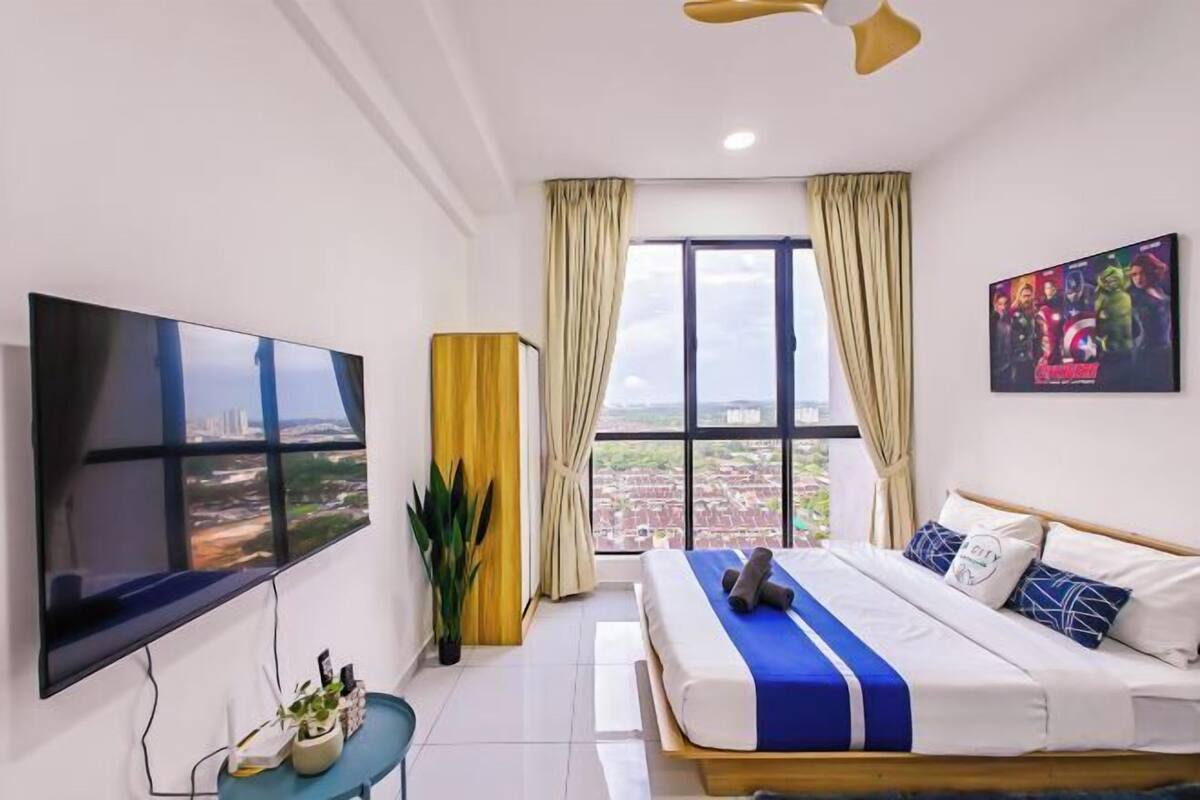Una camera d'hotel con una televisione grande, un letto con biancheria azzurra e bianca, una finestra con tende e vista sulla città.
