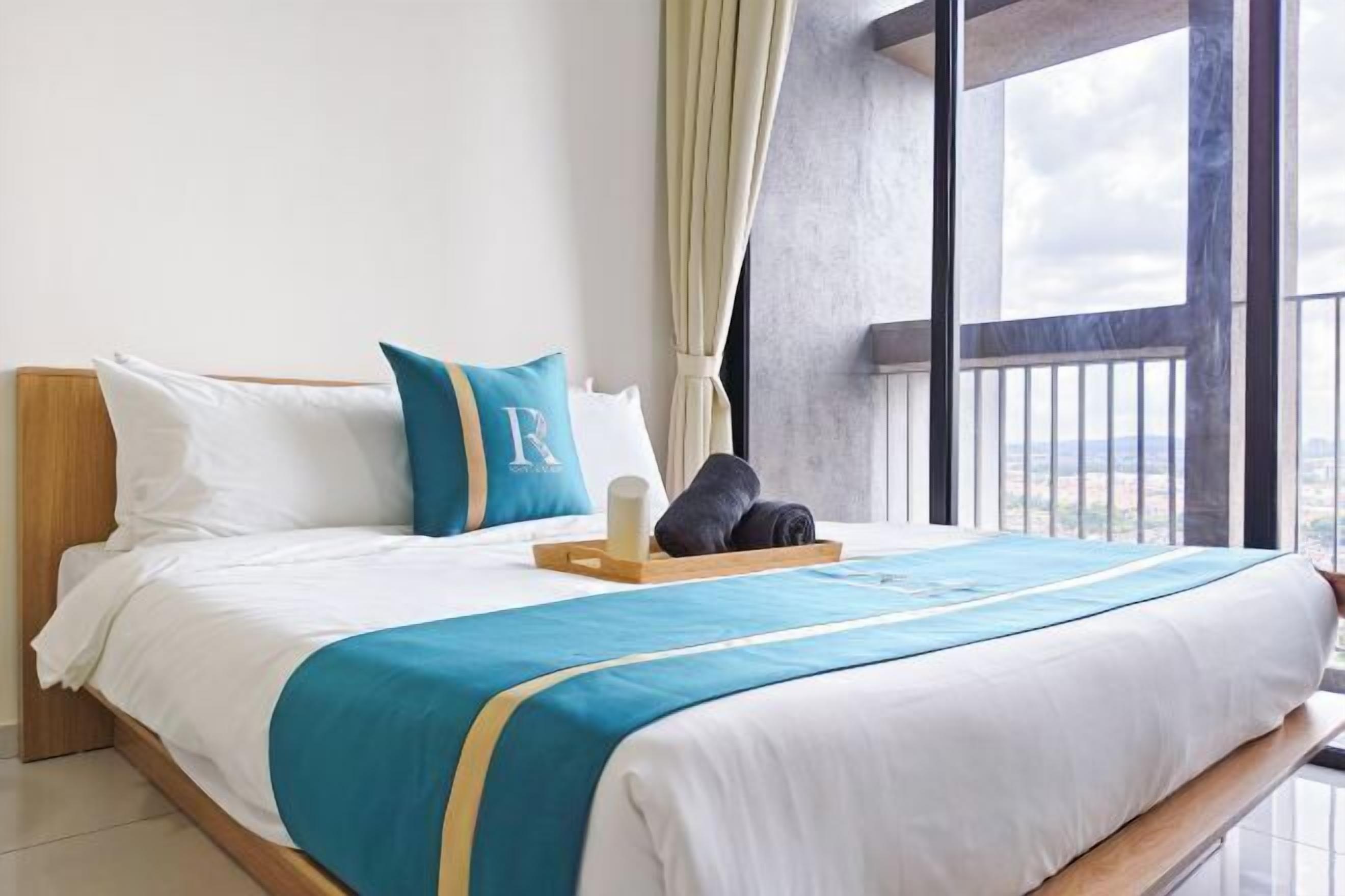 A hotel room with a large bed, a view of the outdoors, a wooden headboard, and a window with curtains.