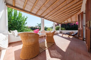 Un espacio de estar al aire libre techado con mobiliario de mimbre, un sofá blanco y una mesa.