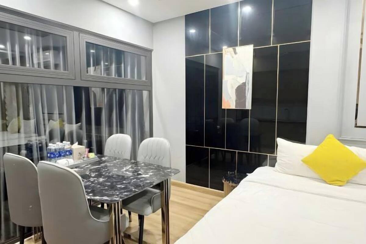 A modern room with a bed, a dining table with chairs, and a large window with curtains.