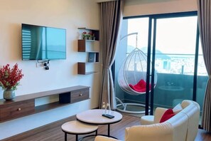 Une chambre d’hôtel moderne dotée d’une télévision à écran plat, d’un canapé, d’une petite table, d’un fauteuil suspendu et d’un balcon avec vue.