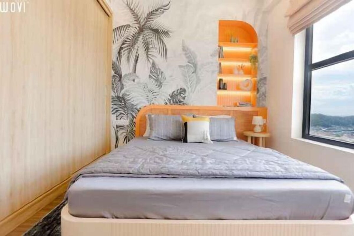 Un dormitorio con cama, una mesita de noche, una estantería con libros y una ventana con vistas.