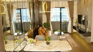 A modern living room with a sofa, a dining table with chairs, a TV, and a large window with curtains.