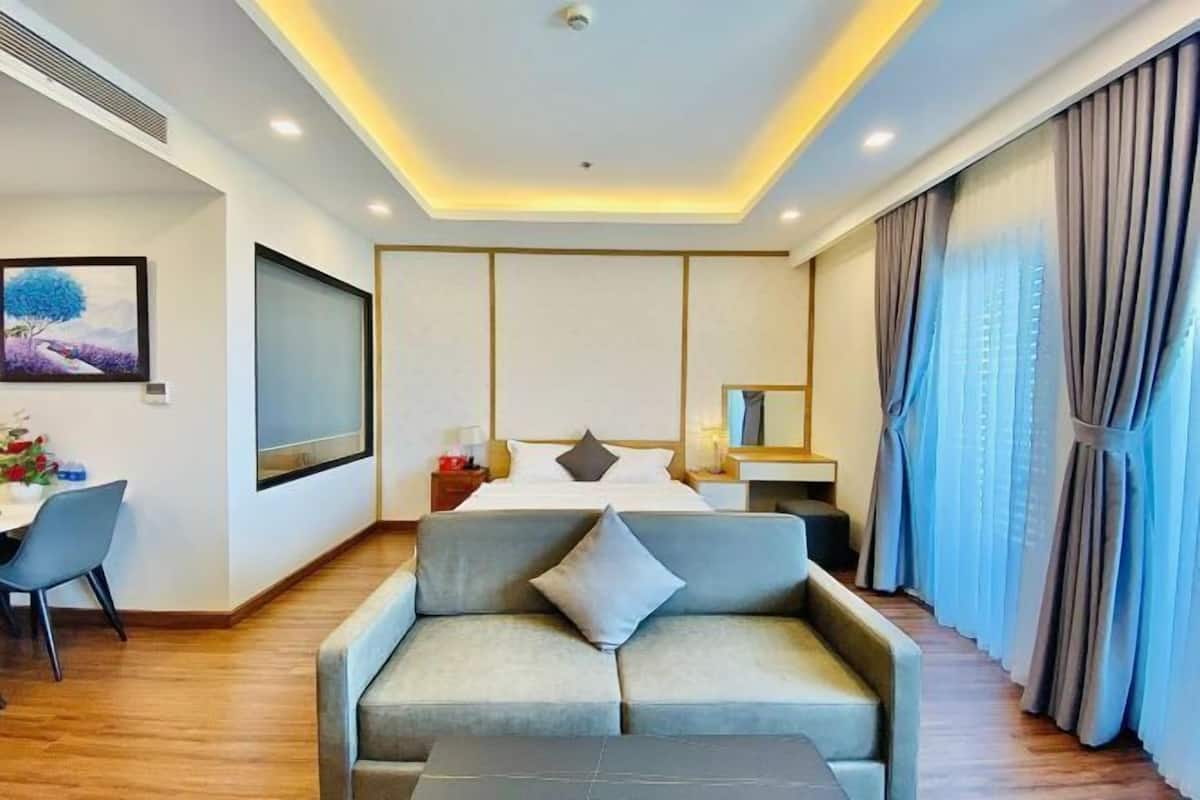 A hotel room with a bed, a sofa, a desk, and a large window with curtains.