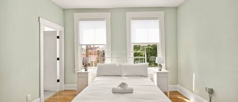 A bedroom with a bed, two bedside tables, a window, and a door.