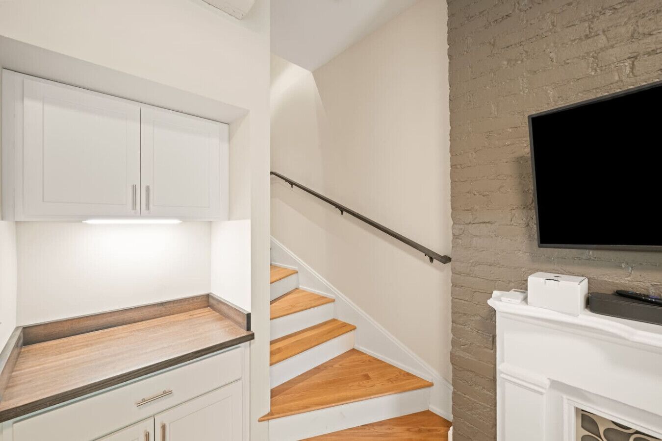 Une cuisine avec des meubles blancs, un plan de travail en bois et un escalier avec des marches en bois et une rampe en métal.