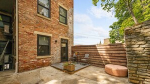 A brick building with a patio area featuring a wooden fence, a stone wall, and outdoor seating. - Hidden Gem 2BD w/ Patio, Near Findlay Market, UC (Cincinnati)
