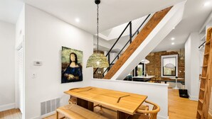 A modern interior with a wooden dining table, bench, and chairs. A staircase with a wooden railing leads to an upper level. - Lux Hidden Gem, 2bd w/ Patio Steps from All OTR (Cincinnati)