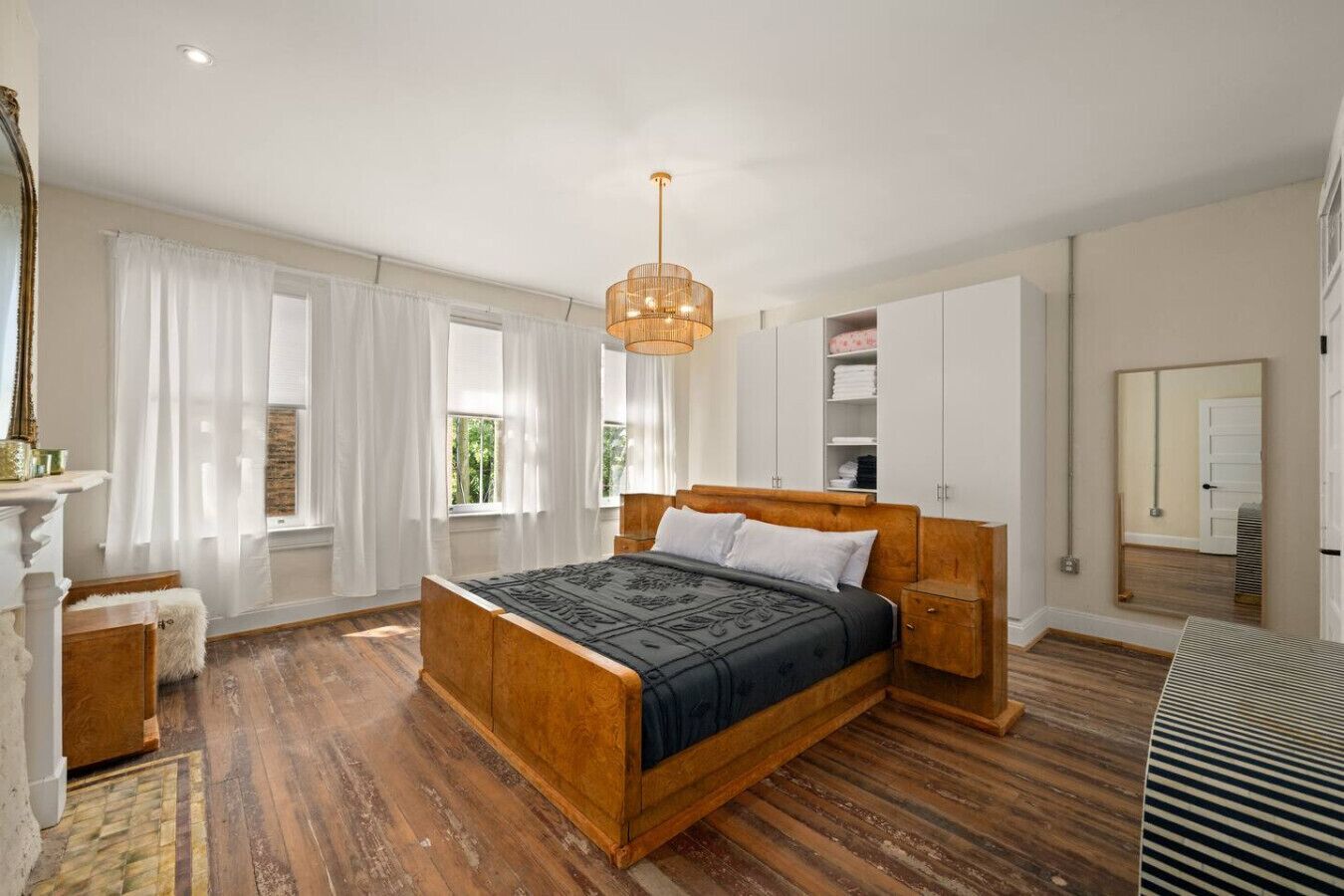 Un dormitorio amplio con una cama de madera grande, una mesita de noche de madera, una lámpara colgante y un armario.