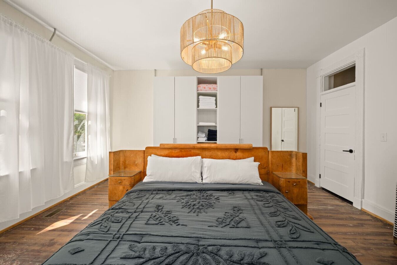 A bedroom with a wooden headboard, a large bed with a patterned bedspread, a hanging light fixture, and built-in wardrobes.