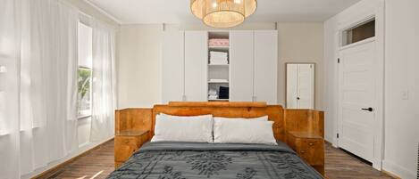 Un dormitorio con cabecera de madera, una cama grande con colcha estampada, una lámpara colgante y armarios empotrados.