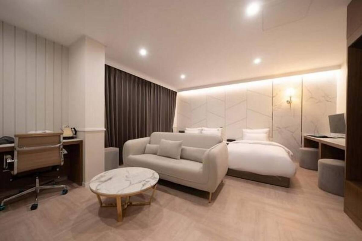A modern hotel room with a sofa, a bed, a desk, and a small round table.