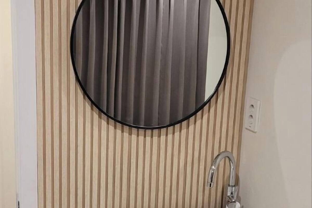 A bathroom with a round mirror, a vertical striped wall, and a modern faucet.