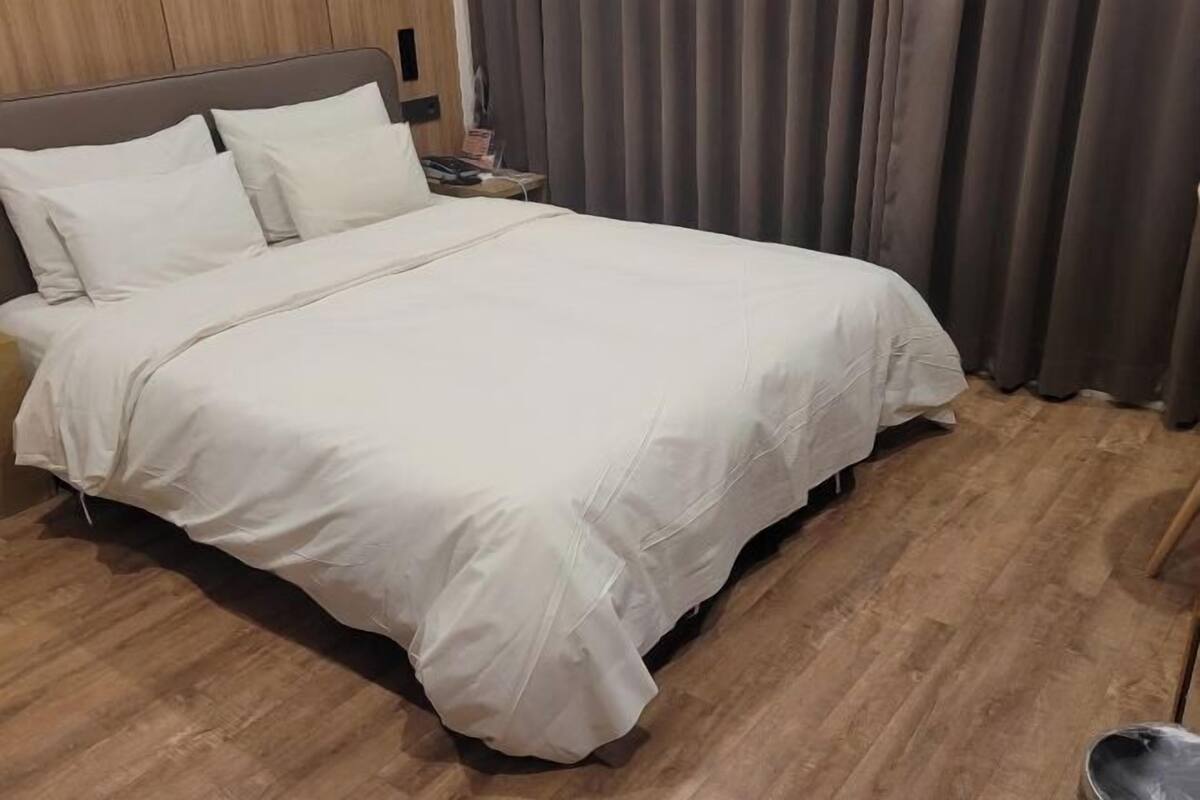 A neatly made bed with white bedding, a wooden headboard, and a nightstand with a lamp and a book.