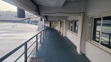 Un pasillo con barandilla metálica, una ventana a la derecha y una puerta al final.