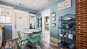 A dining area with a round table and chairs, a coffee station, and a sign welcoming visitors to the beach house. - Sunny Craftsman Cottage Close To Seawall & Strand (Galveston)