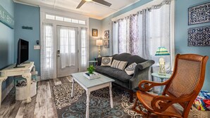 A living room with a sofa, a wooden chair, a coffee table, a television, and a ceiling fan. - Sunny Craftsman Cottage Close To Seawall & Strand (Galveston)