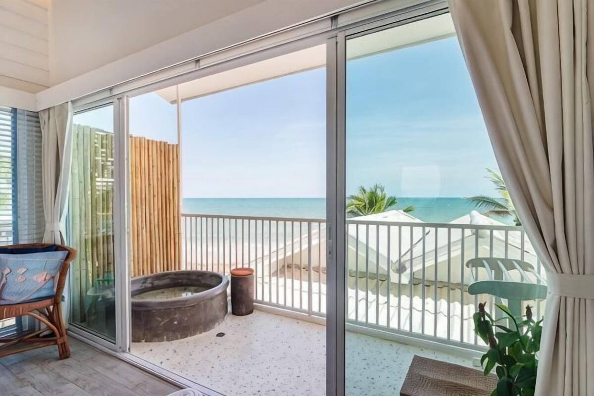 Varanda com vista para a praia, uma cadeira, uma mesinha e um vaso com planta.