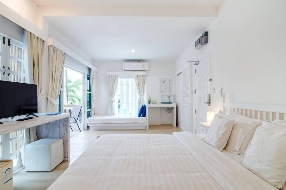 Quarto de hotel com uma cama grande, uma escrivaninha com computador, televisão e janela com cortinas.