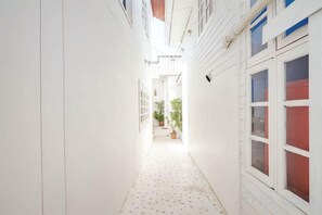 Un pasillo estrecho con piso estampado, paredes blancas y un ventanal con vidrios rojos.
