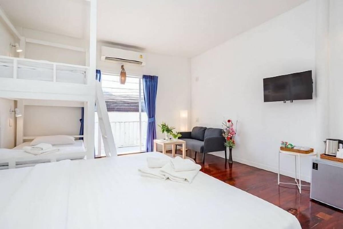 A hotel room with a bunk bed, a sofa, a TV, a small table, and a kitchenette.