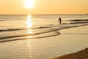 A beach scene with a person walking along the shore during sunset. - Baan Kangmung HuaHin Resort (Hua Hin)