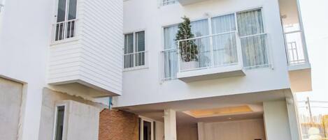 A multi-story residential building with balconies, a brick base, and a visible outdoor seating area.