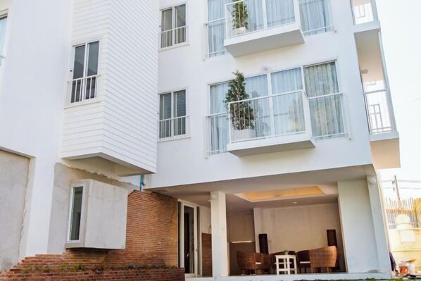 Un edificio residencial de varios pisos con balcones, base de ladrillo y un espacio al aire libre para sentarse.