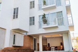 Un edificio residencial de varios pisos con balcones, base de ladrillo y un espacio al aire libre para sentarse.