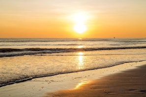 Escena de playa con el sol poniéndose sobre el océano, olas mansas acariciando la orilla.