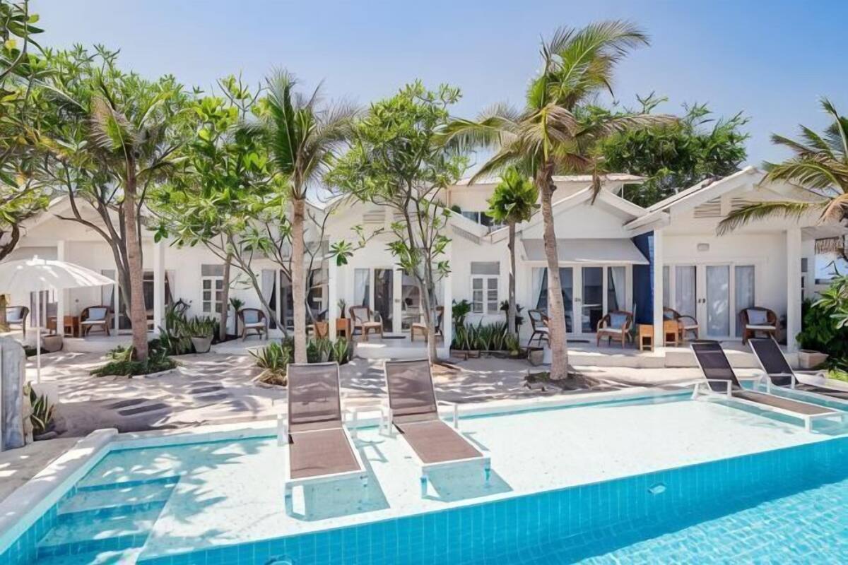 Uma área de piscina com espreguiçadeiras, palmeiras e um céu azul límpido.