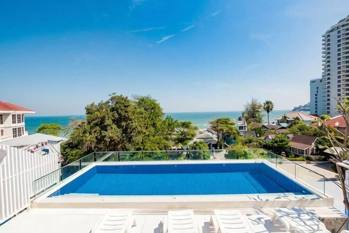 Uma piscina no terraço com água azul cristalina, rodeada por espreguiçadeiras, com vista para uma praia e oceano.