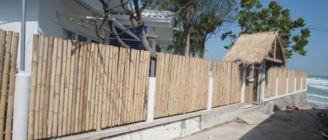 A beachfront property with a wooden fence, a thatched-roof structure, and a white building with a balcony.