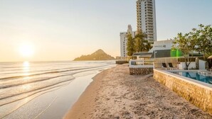 A beachside hotel with a pool, beachfront view, and a tall building in the background. - Baan Kangmung HuaHin Resort (Hua Hin)