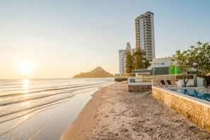 Un hotel sulla spiaggia con piscina, vista sul mare e un edificio alto sullo sfondo.