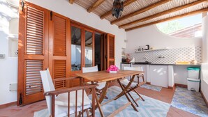 Una mesa de madera con sillas, una cocina con armarios blancos y un salpicadero con diseño, y un ventanal grande.