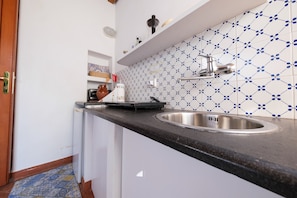 A kitchen with a black countertop, a stainless steel sink, and patterned tile backsplash.