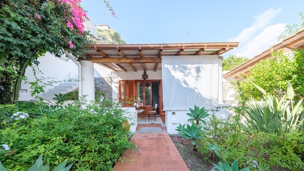 Un sendero de jardín que conduce a un patio cubierto con una pared de piedra y contraventanas de madera.