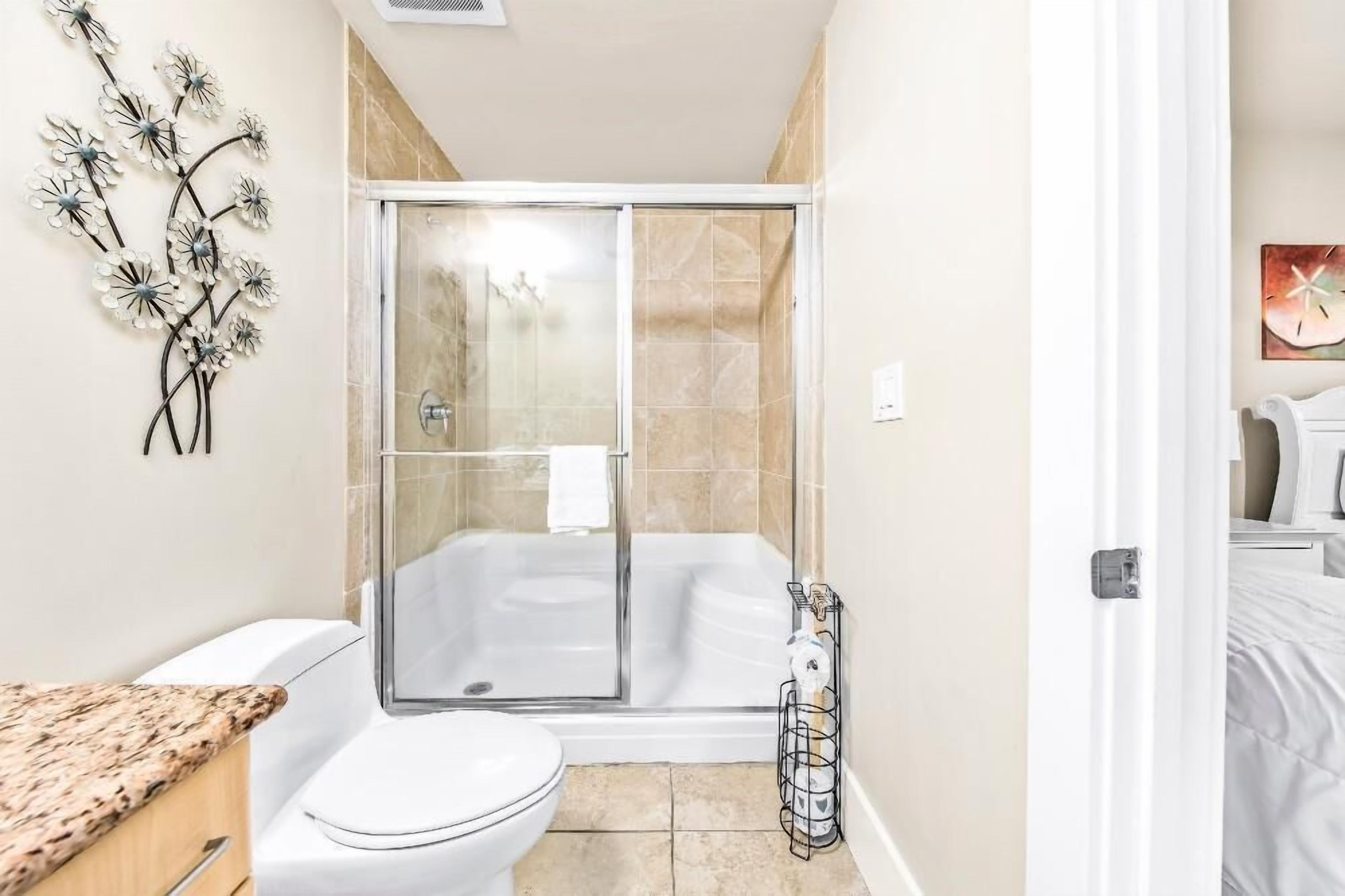 A modern bathroom with a glass-enclosed shower, a white toilet, and a granite countertop.
