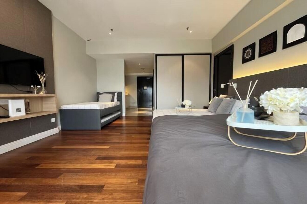 Ein modernes Schlafzimmer mit einem großen Bett, einem Nachttisch mit Lampe und einem an der Wand befestigten Fernseher.