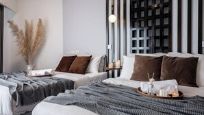 A hotel room with two beds, a decorative wall, a hanging light, and a bedside table with candles.