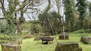 A rustic outdoor setting with a metal tub on a stand, surrounded by moss-covered rocks and dense greenery. - Roselyn House (Par)