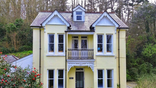 A two-story house with a balcony, a front door, and a small porch area. - Roselyn House (Par)