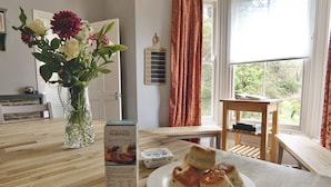 A dining table with a box of Original Cornish Fairings biscuits, a plate of biscuits, and a vase with flowers. - Roselyn House (Par)