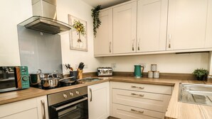 Una cocina moderna con gabinetes blancos, horno empotrado, estufa y microondas. Hay un lavaplatos y una encimera con diversos utensilios de cocina.