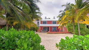 A beachside building with a red facade, surrounded by lush greenery and palm trees. - Casa El Cocal  -  Yucatan Home Rentals (Chicxulub)